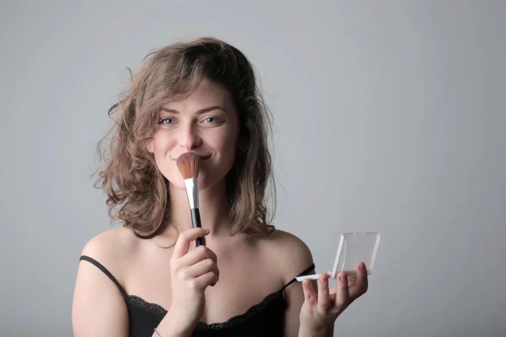 Uśmiechnięta kobieta używa pędzla do makijażu w studio, podkreślając swoją urodę kosmetykami.