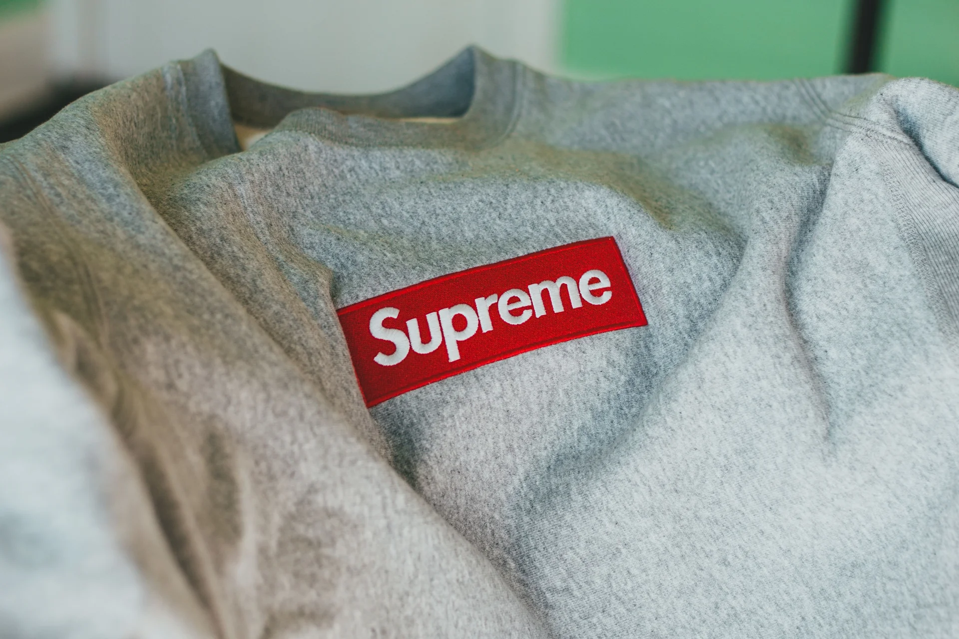 Zbliżenie na szarą koszulkę z wyraźnym czerwonym logo marki Supreme, leżącą płasko.